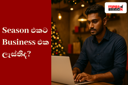 උත්සව සමය | A realistic photo of a young Sri Lankan entrepreneur working on a laptop in a warmly lit shop decorated for Christmas, with festive lights and a tree in the background. The left side features a red panel with Sinhala text reading “Season එකට Business එක ලෑස්තිද?” and the Vyapara.lk logo appears in the top right corner.
