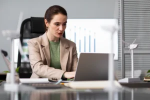 grow | Woman working on a laptop at a modern office desk with wind energy models.