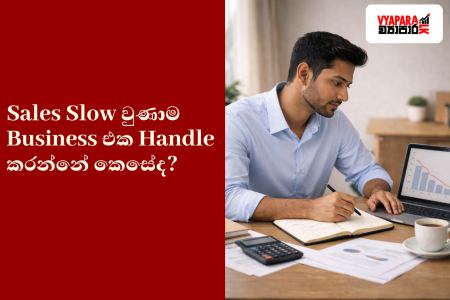 sales slow | A featured image for a Sinhala business article showing a Sri Lankan small business owner analysing sales data on a laptop at a desk, with a red panel containing the Sinhala headline “Sales Slow වුණාම Business එක Handle කරන්නේ කොහොමද?” and the Vyapara.lk logo.