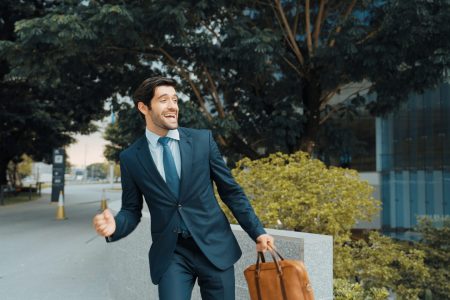 Smart business man walking along the road while holding bag at park. Professional project manager smiling while traveling in lively mood. Happy investor getting a promotion. Business dance Exultant.